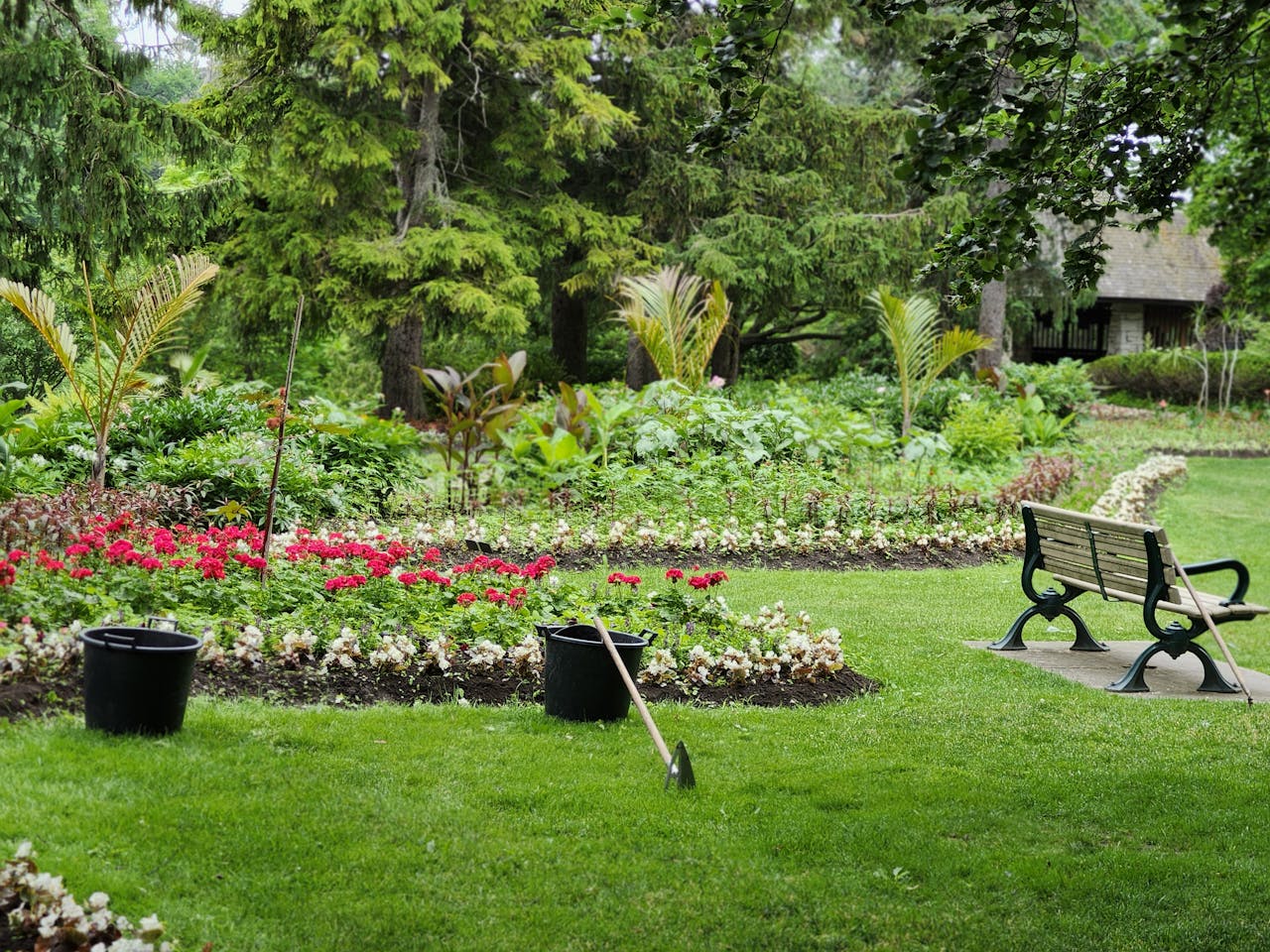 Tranquil park scene featuring lush greenery, a flower garden, and an empty bench.